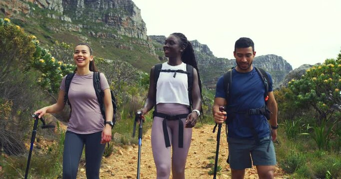Hikers walking down a trail on a mountain with hiking sticks. Diverse group of active and adventurous young friends exploring a rugged path in nature. Happy tourists enjoying a scenic trek outdoors