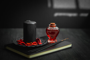 Black leather book, candle, red potion and ritual sticks on a black background.