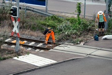 Road workers in orange uniform carry out work at a railway crossing