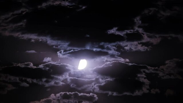 Timelapse of moon moves in the night sky through dark clouds. The mystical moon rises up against the background of clouds. Moonlight shines in the black night sky. Time lapse.