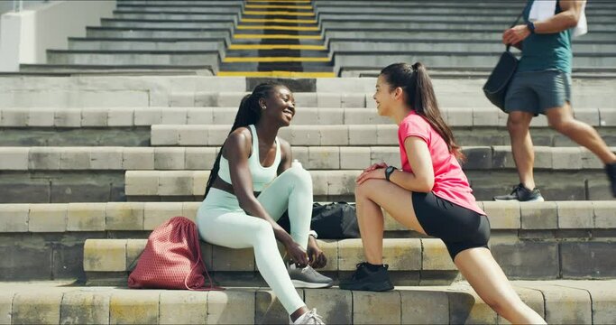 Two motivated female athletes stretching and talking before a workout in sports stadium. Fit, young man high fiving friends after training. Team of active and sporty athletes encouraging one another