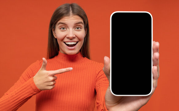 Excited happy young woman pointing finger to blank phone screen with copy space for app
