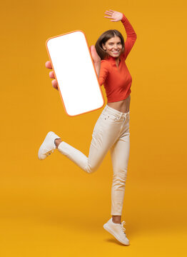 Happy funny young woman jumping and showing blank phone screen with copy space for app