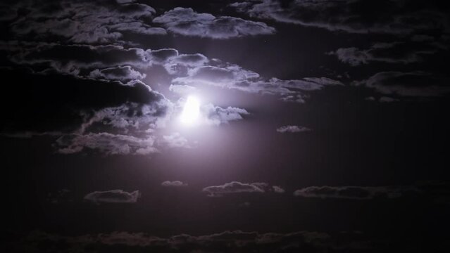 Timelapse of moon moves in the night sky through dark clouds. The mystical moon rises up against the background of clouds. Moonlight shines in the black night sky. Time lapse.