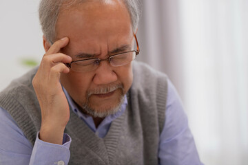 Asian Elderly man with a headache sitting on sofa in living room.