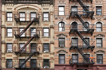 Old fashioned Manhattan apartment building facade with ornate decorative stone carving and external fire escape ladders - 516096513