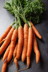 Close up of bunch of carrots with green foliage, on dark background