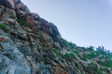Rocky terrain with steep rough cliffs and scattered weeds. Mountain limestone rocks texture