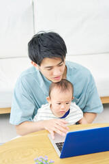 リビングで赤ちゃんとノートパソコンを見る父親