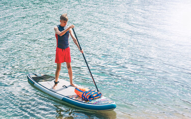 Teenager on a SUP board rakes a wave with an oar. SUP surfing. The concept of an active lifestyle.