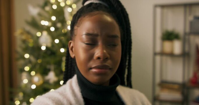 Close-up of an African-looking girl having video chat over the phone with friend. She talks about day, shares impressions and says goodbye. A Christmas tree flickers behind.