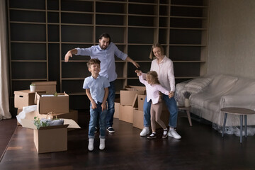 Fototapeta na wymiar Happy active parents teaching two energetic kids to dance at new home, enjoying family party at moving paper boxes, smiling, laughing, having fun, celebrating, house buying, apartment rent, renovation