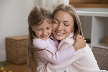 Happy overjoyed young mom cuddling, tightening cute little daughter kid, smiling with closed eyes, enjoying family leisure time, closeness with child, hugging girl with love, tenderness, affection