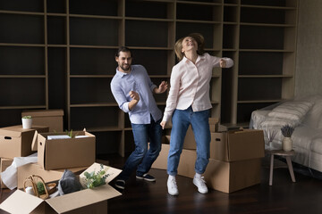 Fototapeta na wymiar Cheerful happy young married couple moving into first home, having fun, dancing at paper boxes, laughing, celebrating house buying, apartment rent. Real estate purchase concept