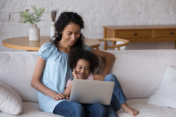 African mom and daughter enjoy movies on laptop relax on sofa looks at screen watch on-line cartoons, amusing content in video vlog, spend leisure at home. Children development use modern tech concept