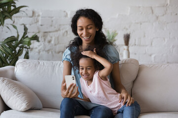 African mom her little daughter have fun hold smart phone using new cool mobile application,...
