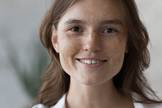 Young woman with natural beauty, non-make-up skin smiling looking at camera, cropped shot. Cute ginger female with charming appearance, nice freckles on her beautiful face close up portrait concept