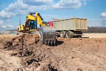 A powerful crawler excavator loads the earth into a dump truck against the blue sky. Development...