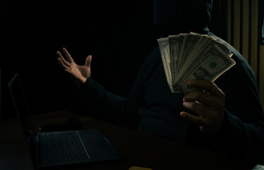 Hands of a man in a hoodie holding money and using a laptop digging into financial data-Internet...