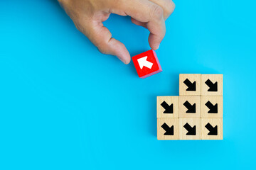 Close-up hand choose cube wooden toy block stacked with arrow icon pointing to opposite directions for way of business change leader planning company and transform concept.