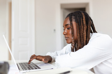 Remote job, technology and people concept - young African business woman with laptop computer and papers working at home office during the Covid-19 health crisis.