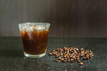 Black coffee ice in a glass with coffee beans on the floor.