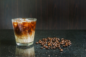 Ready-to-drink black coffee with milk with ice and coffee beans on a black background.