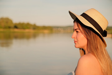 a beautiful girl in a hat stands on the shore. hat in hand.