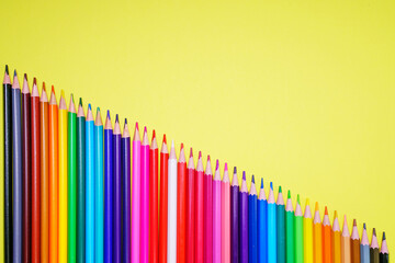Many different colored pencils on a yellow background. Place your text