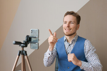 Smiling business man using phone and tripod, making video call for co-workers, sitting in office at...