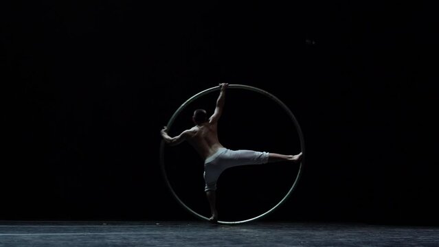 Muscular circus artist perform Cyr Wheel on a black background. Concept of originality, creativity and outstanding