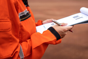 A management person is holding a luxury pen, preparing to take note on paper during perform safety audit at work site. Industrial working scene action photo. Selective focus.