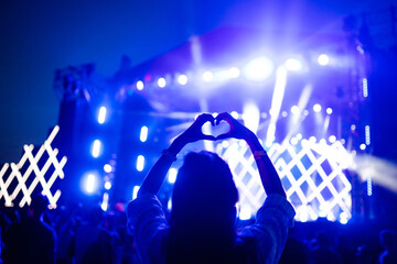 Heart shaped hands at concert, loving the artist and the festival. Music concert with lights and...