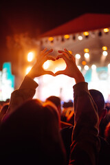 Heart shaped hands at concert, loving the artist and the festival. Music concert with lights and silhouette of people enjoying the concert. - obrazy, fototapety, plakaty