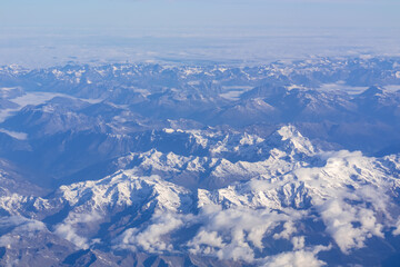 Window view from an airplane on the snow capped mountain ranges of the Alps at the border Austria Italy, Europe, EU. High peak are shrouded in clouds. Flying high above the ground. Freedom