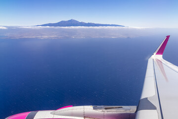 Window view from an airplane on the volcano mountain peak of Pico del Teide on Tenerife, Canary Islands, Spain, Europe, EU. High peak are shrouded in clouds. Flying high above the ground. Freedom