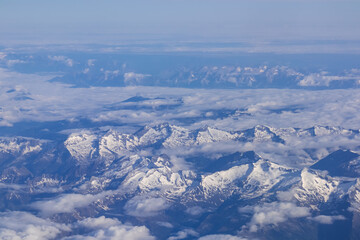Fototapeta na wymiar Window view from an airplane on the snow capped mountain ranges of the Alps at the border Austria Italy, Europe, EU. High peak are shrouded in clouds. Flying high above the ground. Freedom