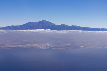 Window view from an airplane on the volcano mountain peak of Pico del Teide on Tenerife, Canary Islands, Spain, Europe, EU. High peak are shrouded in clouds. Flying high above the ground. Freedom