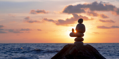 Pile of Stones in Zen style with the sun at sunset by the sea