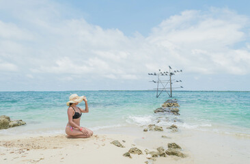 Mujer jóven en traje de baño sentada en la playa soleada con el mar caribe Colombiano de Cartagena al fondo