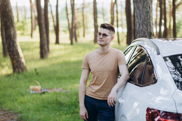 young handsome smiling man holding charging cable at electric charging station point standing near his new car , looking satisfied.
