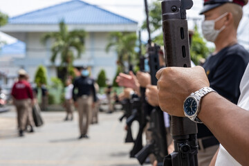 A close-up view of the arm of a Thai policeman, adorned with a wristwatch, is carrying an antique wooden long-barrelled gun.