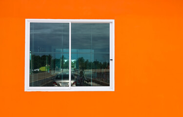 The orange concrete wall background of the building and the white windows with transparent glass reflect.