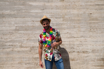 Handsome young man wearing a shirt with Hawaiian flowers, a hat and a necklace with coloured...