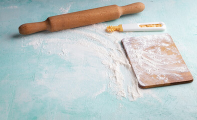 Rolling pin, cutting board, dough cutter with flour on blue background. Bakery accessory. With copy...