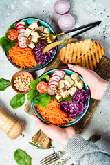 Female hands holding a bowl of vegan lunch: tofu cheese, spinach, cabbage, radishes and carrots. The concept of healthy eating. Top view.