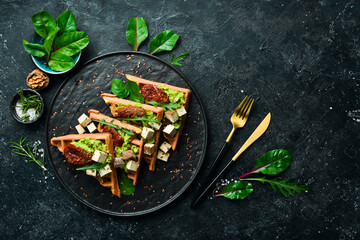 Sandwich for Breakfast. Belgian waffles with avocado pate, sun-dried tomatoes and tofu cheese. The concept of dietary nutrition. On a stone background.