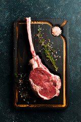 Dry aged raw tomahawk beef steak with ingredients on a black stone background. Top view. Flat Lay.