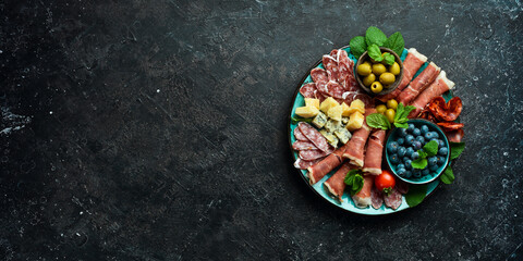 Italian snacks. Plate with cheese and ham, prosciutto, jamon salami, and snacks. On a black stone background.