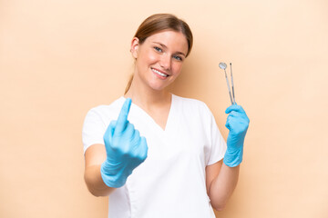 Dentist caucasian woman holding tools isolated on beige background doing coming gesture